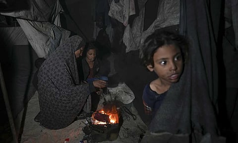 Shireen Daifallah, who was displaced with her children from northern Gaza, checks the fire next to their tent at a camp for displaced people in Deir al- Balah (AP)