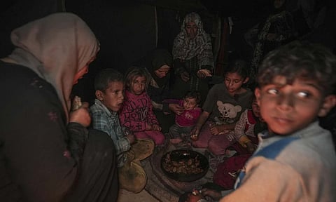 Amani Abu Zarada, fourth from left, feeds her children outside their tent in a camp in Khan Younis, Gaza Strip on Dec19 (AP)
