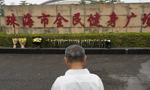 A man stands near flowers laid outside the Zhuhai People's Fitness Plaza, where a man rammed his car into people exercising at the sports center in Zhuhai, in southern China (AP Photo)