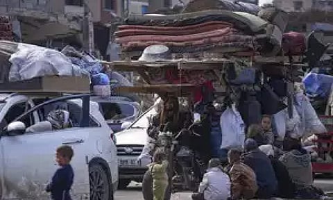 Displaced Palestinians with their belongings gather near a roadblock on Salah al-Din Street