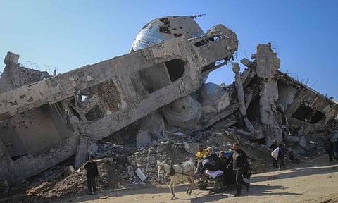 A family rides in a horse-drawn cart past a destroyed mosque in Beit Lahia, northern Gaza Strip (AP)