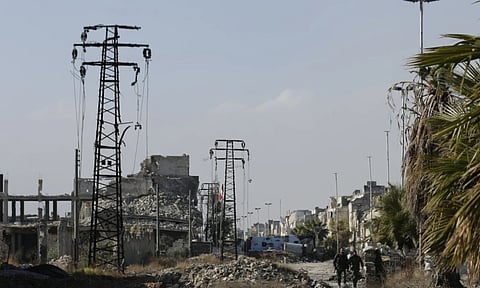 Syrian army soldiers walk next to damaged electricity transmission towers on their way back from the frontline of fighting (AP)