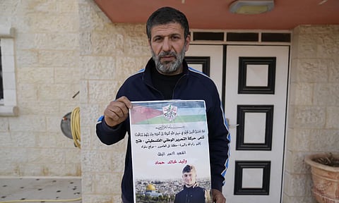 | Khalid Ahmad holds a poster of his 17-year-old son, Waleed, who died in an Israeli prison, that reads in Arabic, "The hero prisoner Martyr, mercy and eternity for our righteous Martyrs," in the West Bank town of Silwad, northeast of Ramallah (AP)