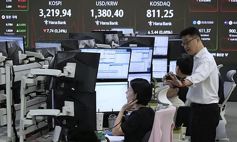Currency traders work near a screen showing the Korea Composite Stock Price Index (KOSPI), top left, and the foreign exchange rate between U.S. dollar and South Korean won, top center, at the foreign exchange dealing room of the Hana Bank headquarters in Seoul, South Korea, Friday, Aug. 8, 2025 (AP) 