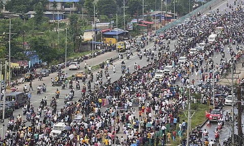People gather as a flower-decked ambulance carrying mortal remains of popular Assam singer Zubeen Garg along with other vehicles proceeds towards his Kahilipara residence from the airport, in Guwahati, Assam, Sept. 21, 2025. (PTI Photo)