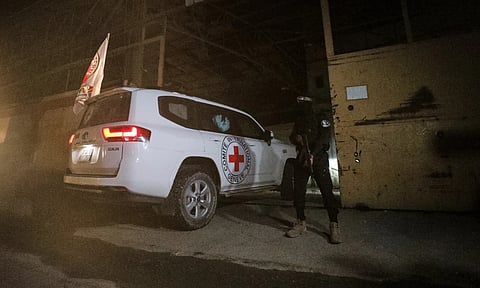 A gunman wearing the uniform of the al-Qassam Brigades, the military wing of Hamas, stands guard as Red Cross vehicles enter a warehouse allegedly to collect coffins containing the bodies of four deceased hostages in Gaza City (AP)