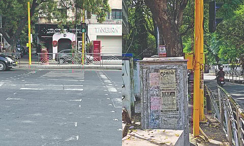 At Ambika Appalam signal in Adyar, space to cross the road from the pavement located metres away from zebra crossing; traffic poles and EB junction box block access on the pavement in RA Puram