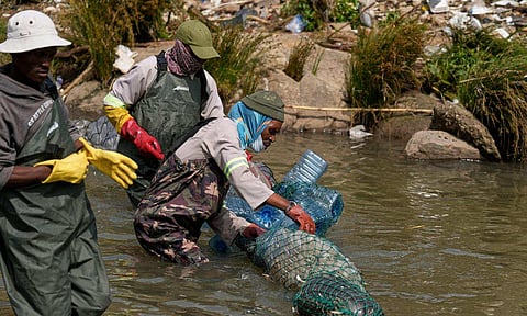 Volunteers wearing wetsuits untangle a long garbage net on the Jukskei River in the Alexandra township in Johannesburg, South Africa