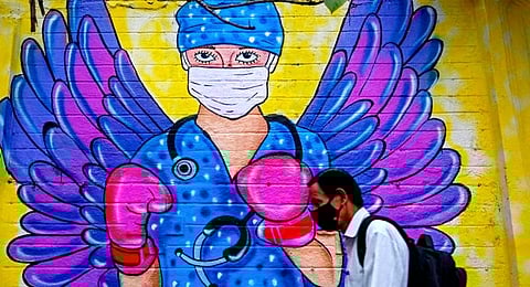 A pedestrian walks past a wall mural depicting a health worker