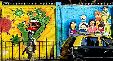 A pedestrian walks past a wall mural depcting the Covid-19 coronavirus in Mumbai
