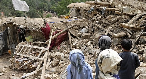 Afghan children stand near a house that was destroyed in an earthquake