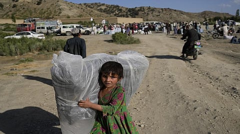 Afghan girl carries a donated matrace after an earthquake in Gayan village