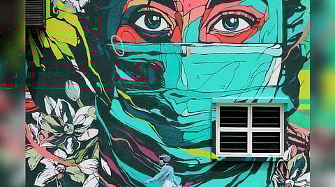 A medical worker wearing personal protective equipment passes by a frontliner mural outside a clinic