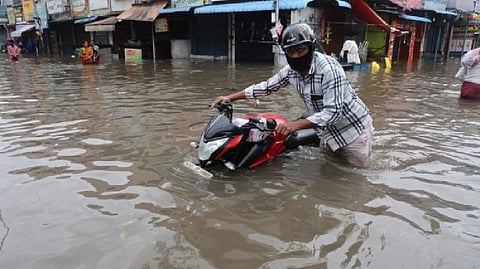 A biker moving his bike through an inundated road.