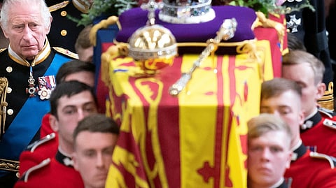 Pall bearers carrying the mortal remains of the Queen with King Charles standing behind.