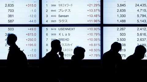 Passersby are silhouetted as they walk past in front of an electric stock quotation board outside a brokerage in Tokyo