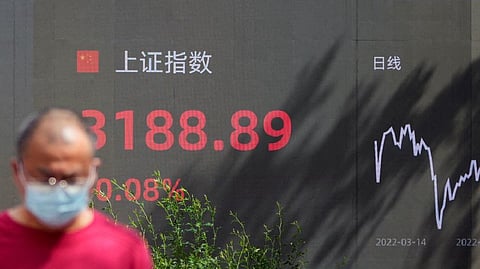A pedestrian walks past a giant display showing the Shanghai stock index