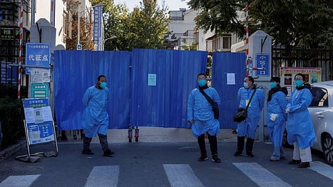 Officials wearing protective aprons stand outside the boarded-up gate of a residential compound