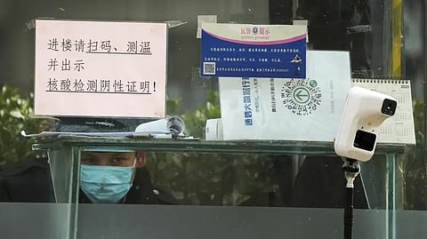 A Security guard keeps watch inside a booth displaying a temperature scan device and a travel QR code, outside an office building in Beijing.