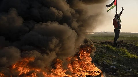 Palestinians burn tires and wave the national flag during a protest