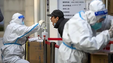 A worker wearing a protective suit swabs a man's throat for a Covid test at a testing site in Beijing.