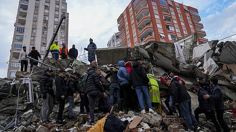People and emergency teams search for people through the rubble of a destroyed building in Adana, Turkey, Monday,