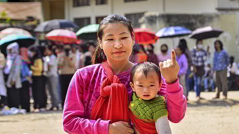 Woman carrying a kid shows her ink-marked finger after casting her vote for the Nagaland Assembly elections, at a polling station in Dimapur, Monday, Feb. 27, 2023