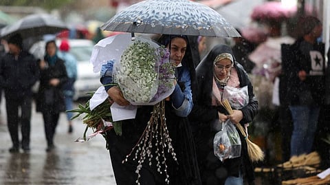 Iranian women walk through rain in a flower market, ahead of Nowruz, the Iranian New Year, in Tehran.