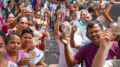 People wait in queues at a polling station to cast their votes for the Karnataka Assembly elections
