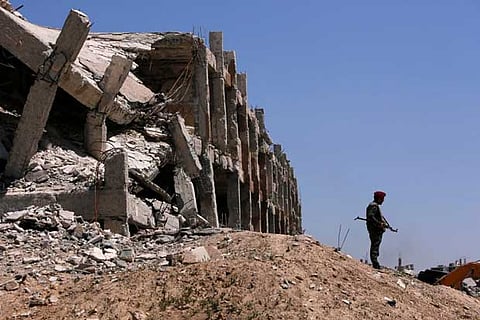 Syrian forces of President Bashar al Assad stands guard near destroyed buildings