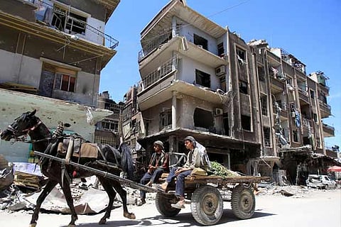 People ride a horse along a damaged street at the city of Douma in Damascus