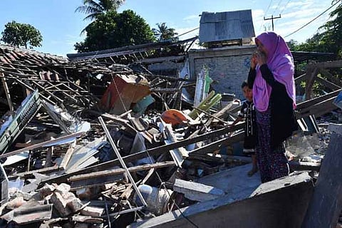 A woman and boy watch as men clear the wreckage of houses damaged by an earthquake in North Lombok