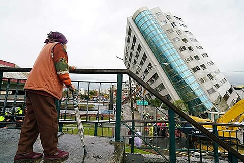A local resident looks out at a building leaning at a precarious angle in Hualien