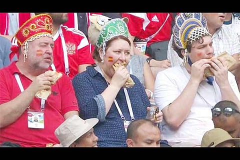 Three fans are seen snacking hot dogs during extra-time in the match between Russia and Spain