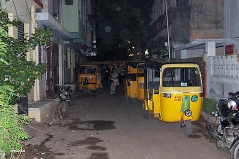 Autorickshaws parked haphazardly in front of residential buildings near the liquor shops