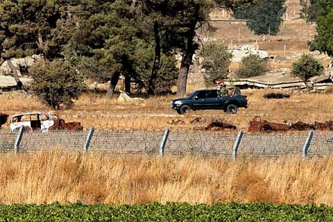 Uniformed men ride a pick-up truck as they carry a Syrian flag in Quneitra