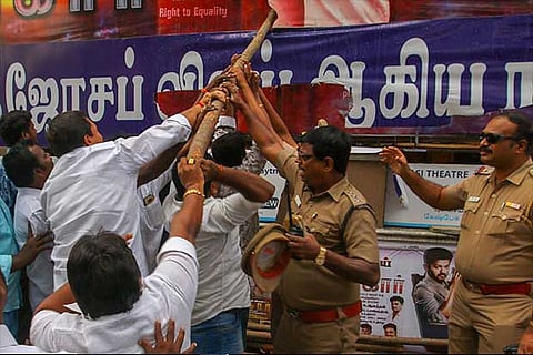 A police officer tries to stop protesters from damaging banners of the film