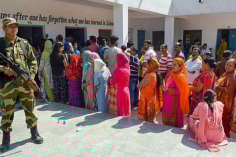 A security personnel stands guard as people wait in queues to cast their votes at a polling station