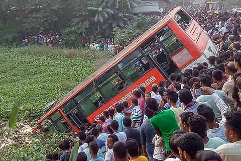 People look on at an Assam State Transport Corporation (ASTC) bus which fell into a pond