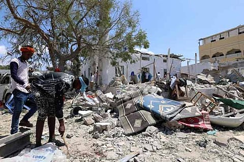 Civilians look at the debris at the site of a blast in the district office of Hawlwadag in Mogadishu