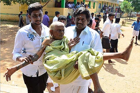 An elderly woman being carried by two men to a polling booth at a government school in Thanakankulam