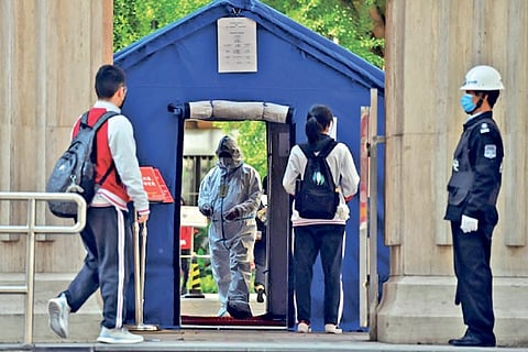 An official in a hazmat suit greets students returning to classes as schools re-open in Beijing