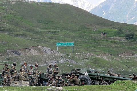 Indian soldiers rest next to artillery guns at a makeshift transit camp before heading to Ladakh