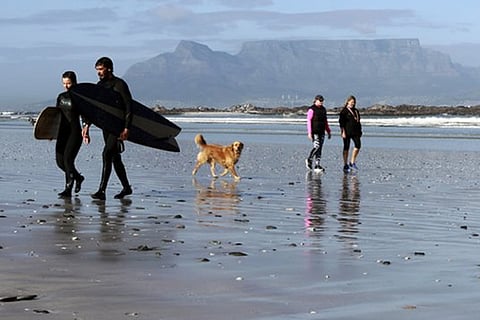 People walk on a beach, with Table Mountain in the background, in Cape Town, South Africa