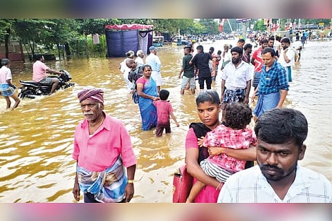 Residents moving in knee deep water on a flooded road in Manapparai on Monday