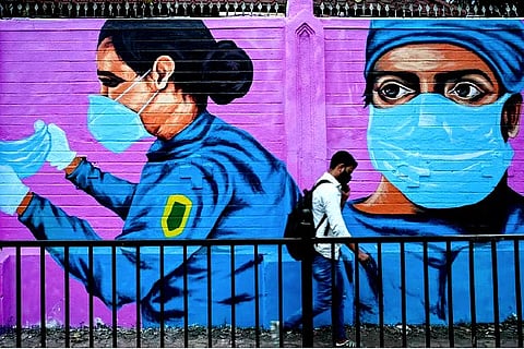 A pedestrian walks past a wall mural depicting health workers (Credit: AFP)
