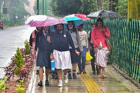 Students use umbrellas to protect themselves from rain, in Bengaluru (Image credit: PTI)