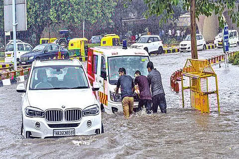 People try to push an ambulance after heavy rain near AIIMS Hospital in New Delhi, on Tuesday