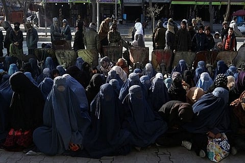 Afghan people sit on the ground in front of a bakery waiting to receive bread in Kabul (Reuters)