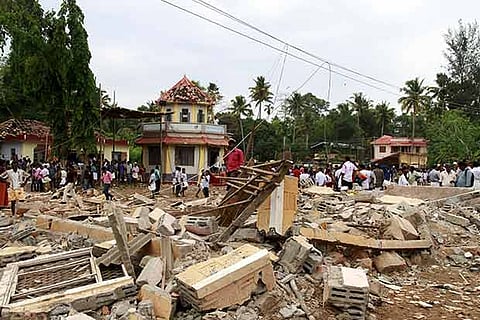 People walk past debris resulting from a fire that broke out at a temple in Kollam in Kerala.